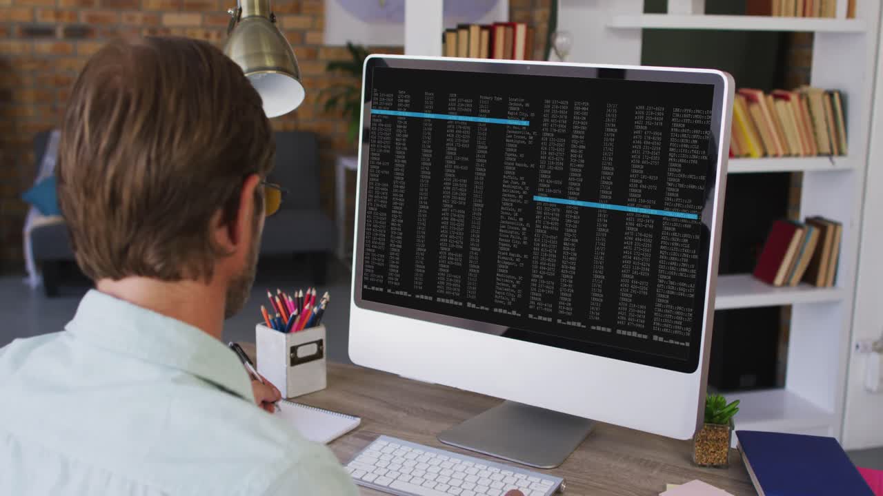 Caucasian man sitting at desk watching coding data processing on computer screen