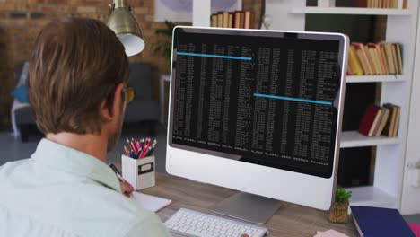 hombre caucásico sentado en un escritorio viendo el procesamiento de datos de codificación en la pantalla de la computadora