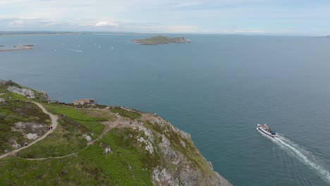 boat sailing on the sea near a large green mountain on a bright sunny blue day