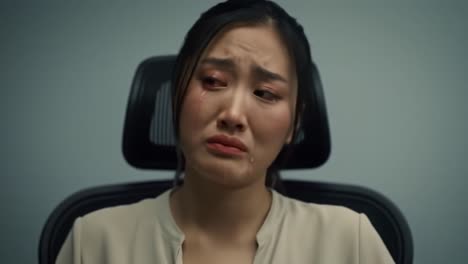 a woman expresses deep distress while sitting in a stark interrogation room. her fear and vulnerability are palpable as she reacts to intense questioning, evoking strong emotions.