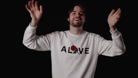 trendy young man waving into camera with both hands, wide, black background