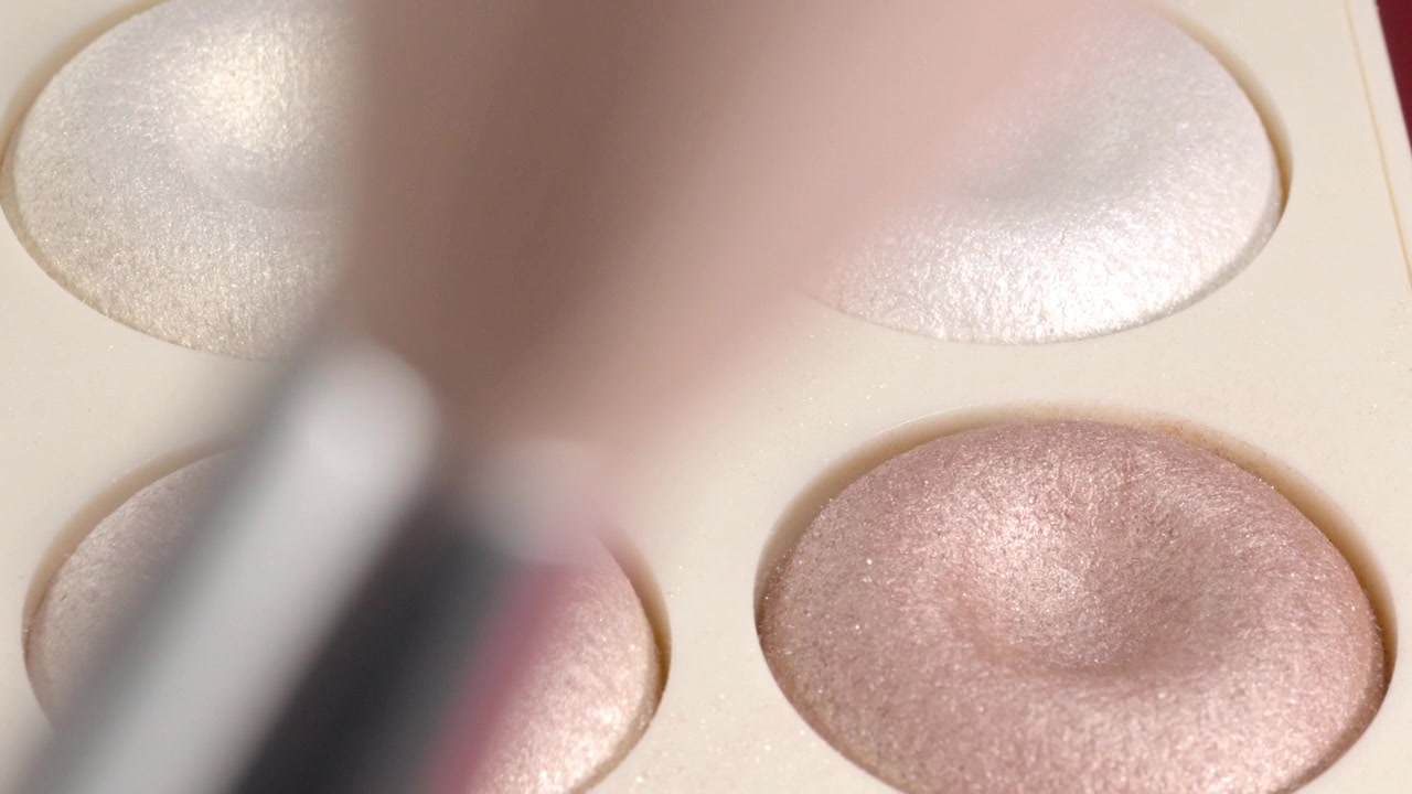 Rack focus shifting from makeup brush to shimmering eyeshadow palette, revealing cosmetic powder texture and metallic beauty shades in closeup