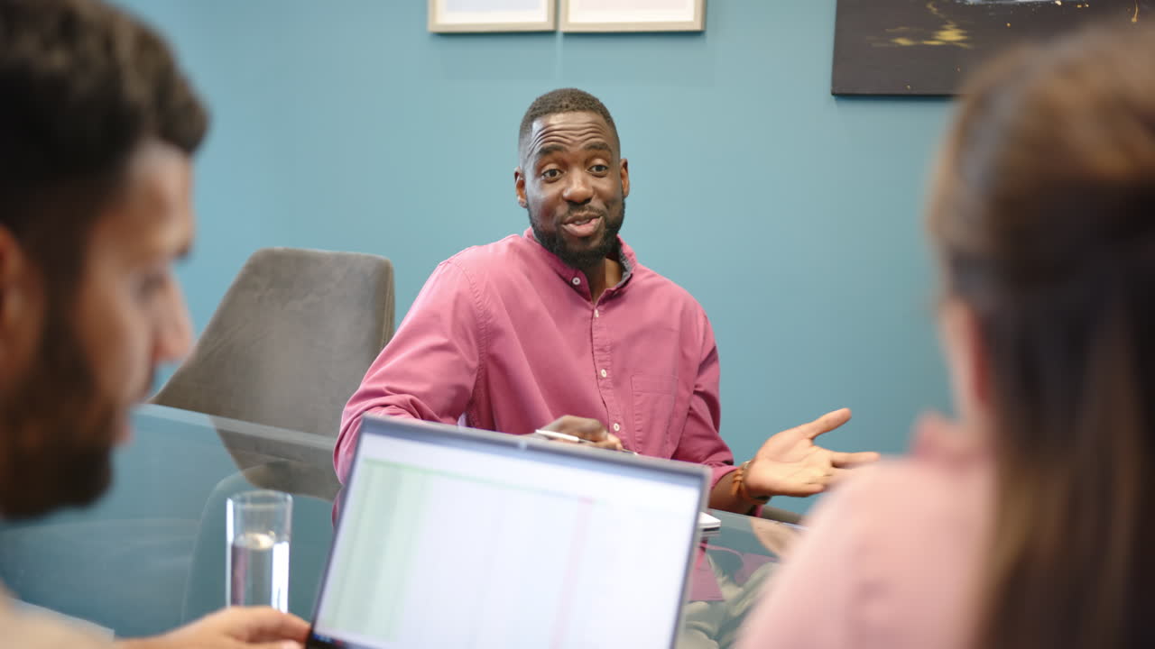 Smiling african american man in pink shirt having meeting with multiracial colleagues in office