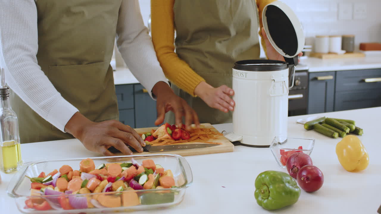 Preparing vegetables and composting scraps, multiracial couple working in modern kitchen, at home
