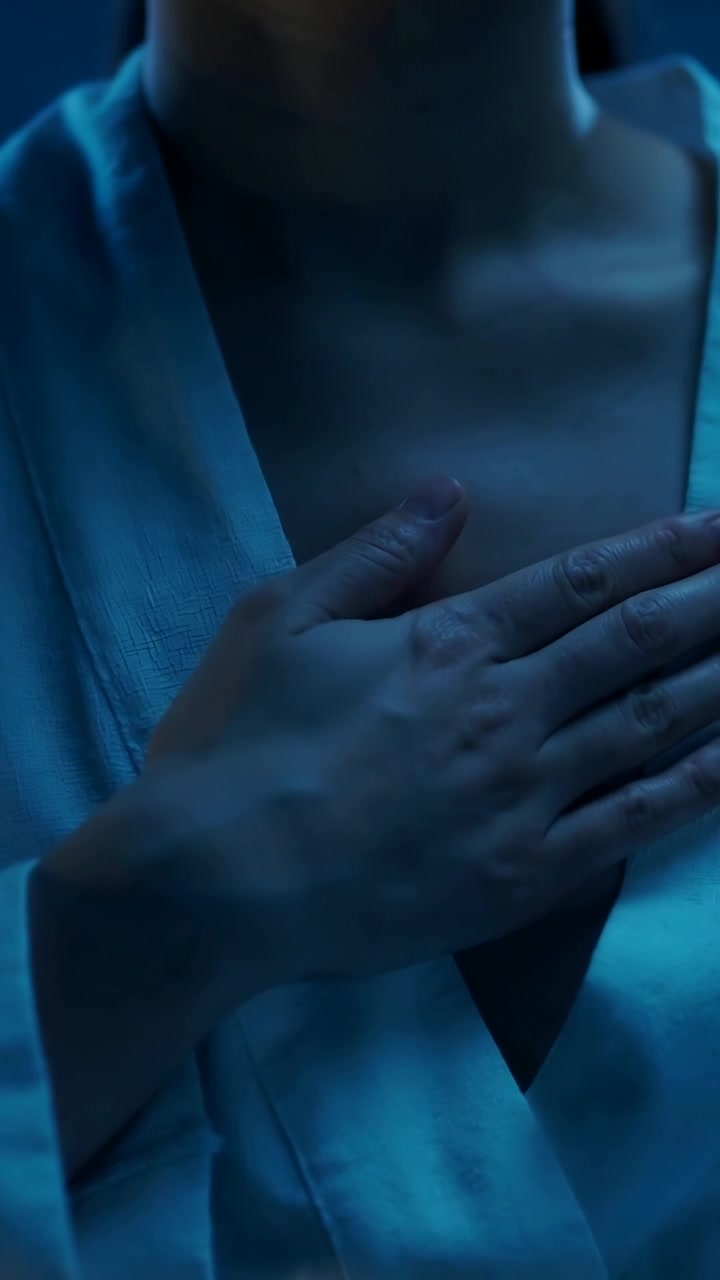 Vertical video: Starting woman placing hand flat over left clavicle at home, robe for comfort