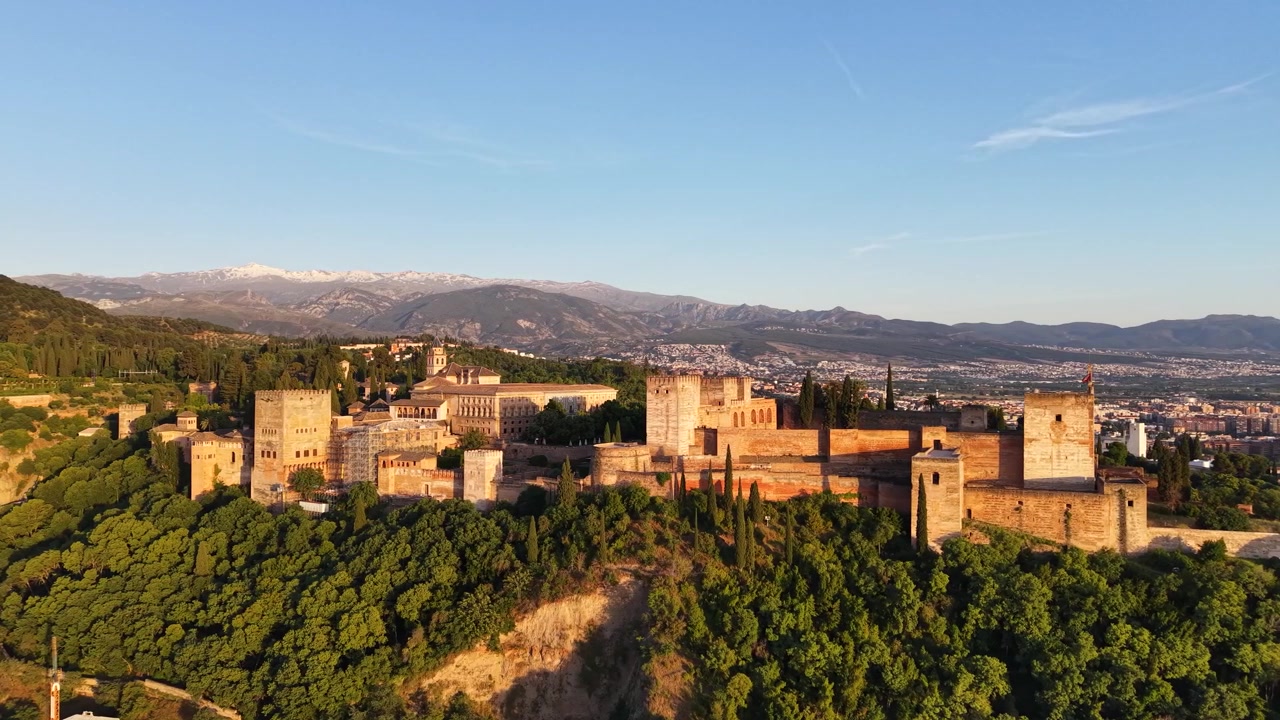 Vista aérea de drone da Alhambra em Granada, Espanha, durante a hora dourada, com luz solar quente na fortaleza e as montanhas nevadas da Serra Nevada.
