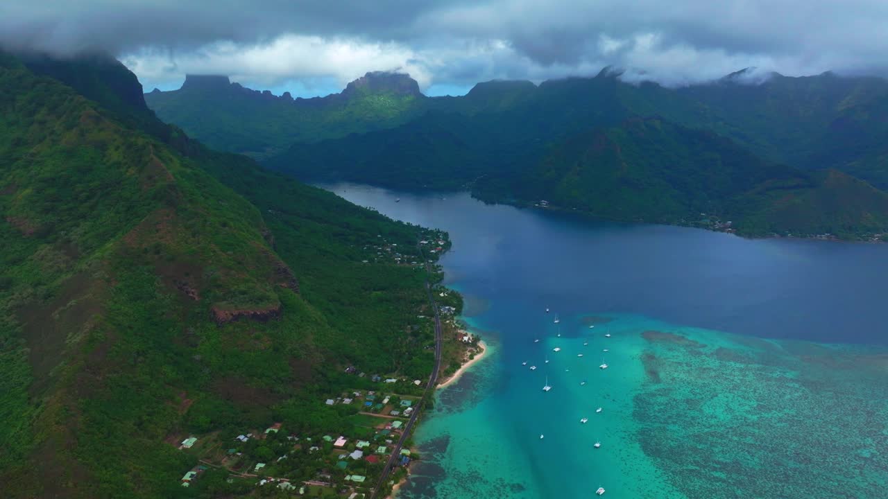 Opunohu Bay in Moorea, French Polynesia, Aerial drone view of with turquoise lagoon water, sailboats, tropical shoreline, and jagged volcanic peaks under dramatic clouds circle right motion