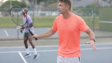 two diverse male friends playing doubles returning ball on outdoor court in slow motion