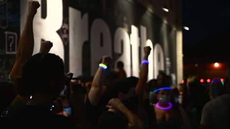 people at a nighttime protest with raised fists and a 'breathe' mural