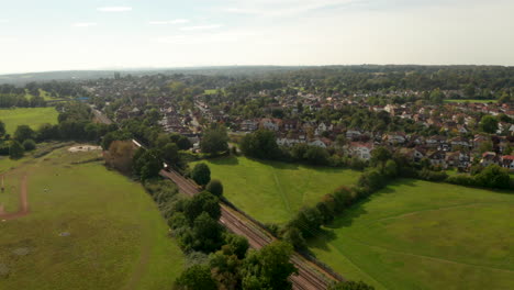 Descending-aerial-shot-of-London-Underground-train-leaving-Theydon-Bois-town