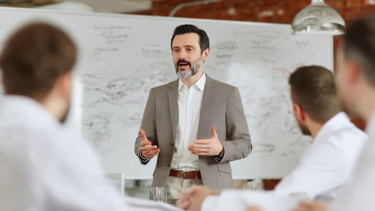 Engaging Business Presentation: A Professional Man Speaks to an Audience in a Bright Modern Office Setting, Illustrating Key Ideas with Enthusiasm and Clarity