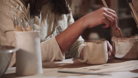 young woman potter working in art studio - painting the final ceramic product from the inside