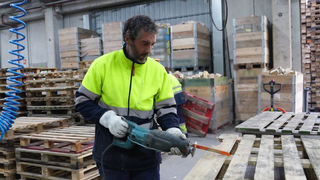 Man working with a power saw in a warehouse full of wooden pallets