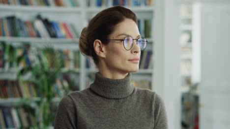 Portrait-Of-The-Attractive-Woman-In-The-Glasses-Looking-At-The-Side-And-Then-Smiling-Nice-To-The-Camera-In-The-Room-With-Books