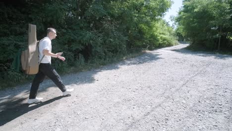 young man walking with guitar on street near forest