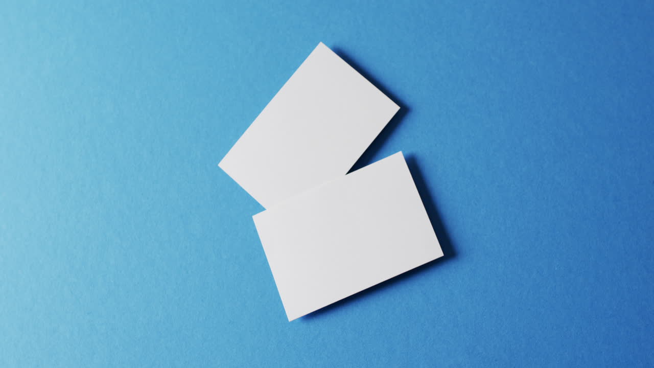 vista aérea de tarjetas de visita blancas y blancas sobre fondo azul, espacio de copia, cámara lenta