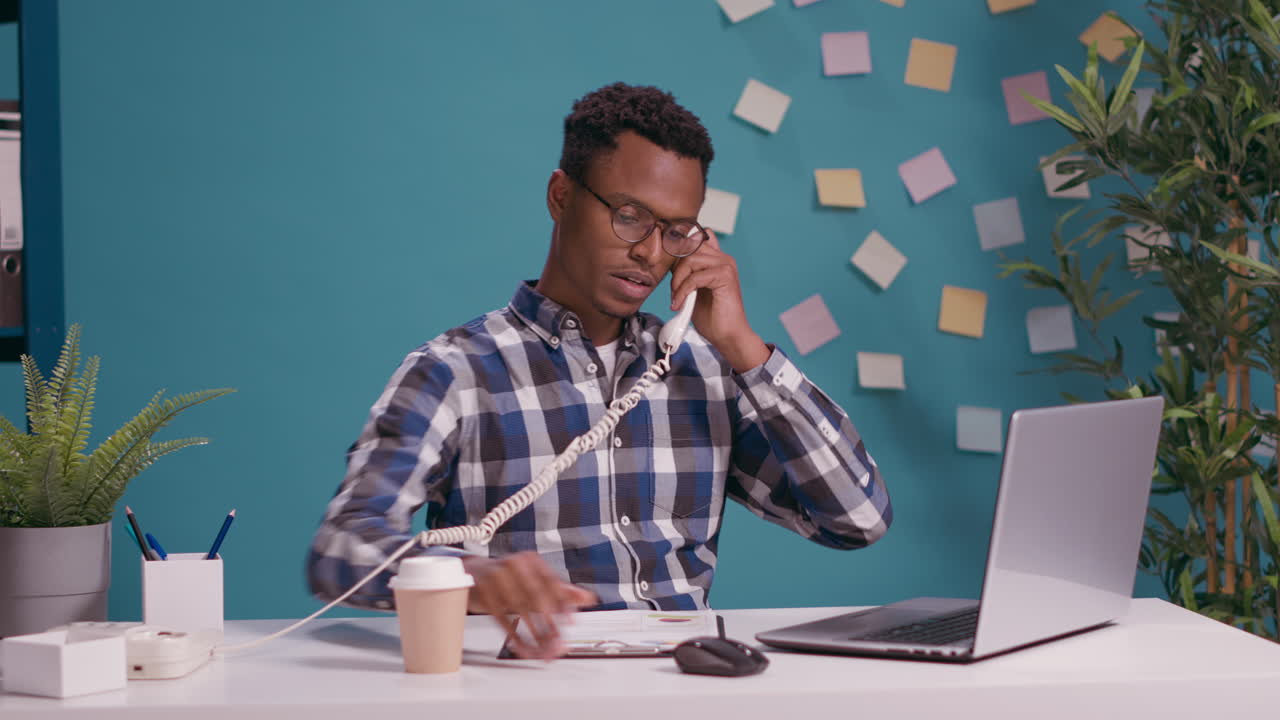 Male secretary answering landline phone at desk with laptop