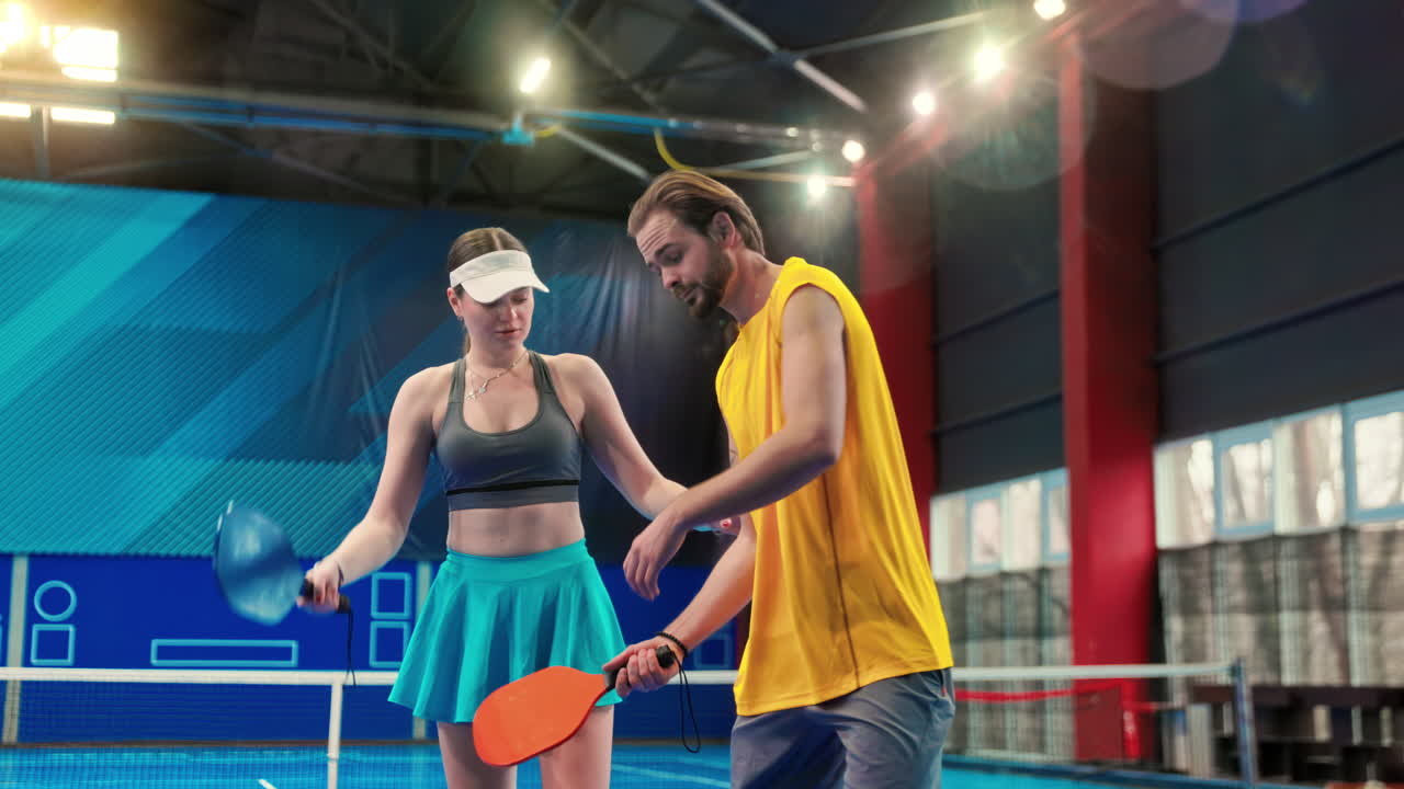 A man teaching a woman how to play pickleball in an inside court