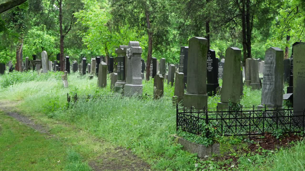 La camera esegue una panoramica sul Wiener Zentralfriedhof, mostrando lapidi e sentieri