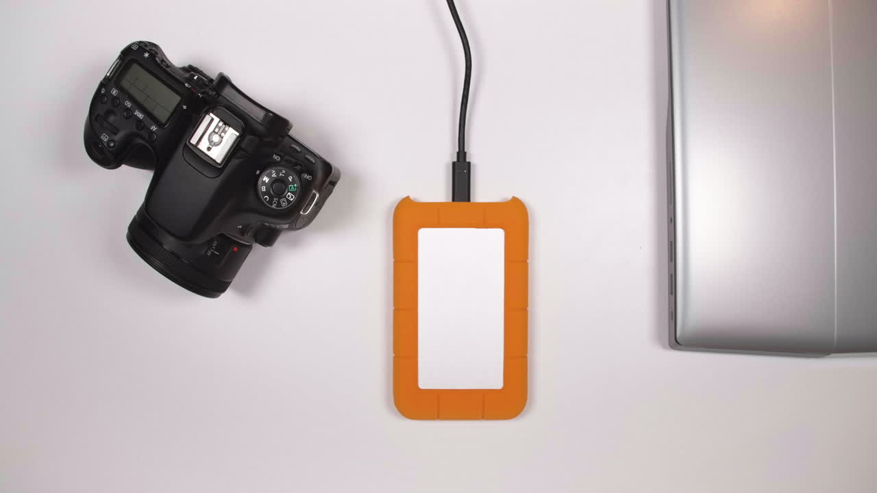 la mano del hombre quita el cable del disco duro de la computadora portátil: cierra la computadora portátil y guarda el disco duro externo y la cámara dslr de la mesa