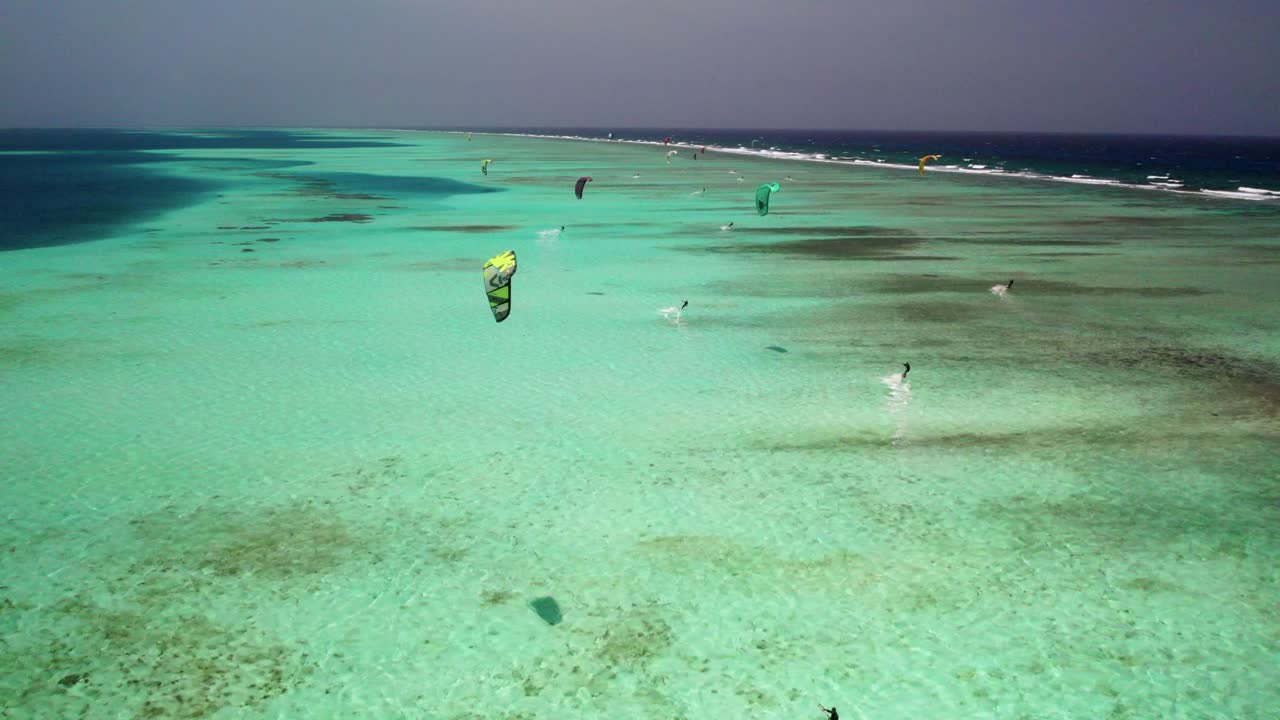 kite surfers en los rocas arrecife de coral, vibrantes aguas turquesas bajo un cielo despejado, vista aérea