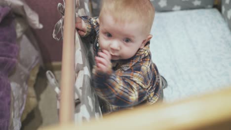 little-kid-with-blue-eyes-plays-at-bed-edge-near-pink-wall