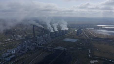 Landscape view with a coal-fired power station with its chimneys and funnels releasing white smoke into the air on a sunny and cloudy day