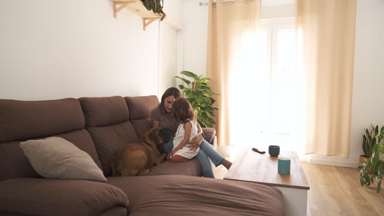 Smiling mother and daughter caressing dog on sofa at home