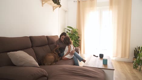 smiling mother and daughter caressing dog on sofa at home