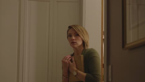 a scared woman is seen looking around a doorway while holding a book.