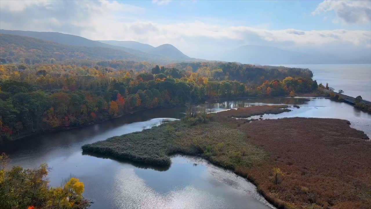 volando sobre pantanos, un río y follaje de otoño hacia montañas y colinas distantes