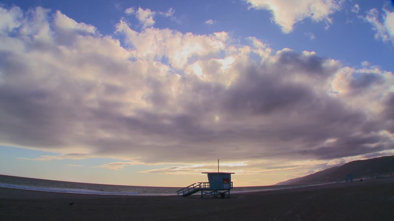 lapso de tiempo de formaciones de nubes moviéndose detrás de una estación de salvavidas en una playa de los ángeles