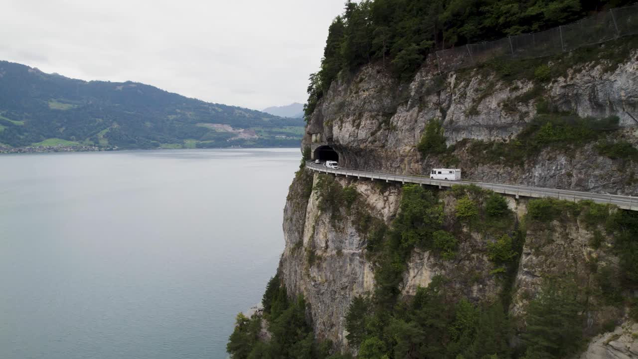 campista conduciendo a lo largo de un camino de acantilado con vista al lago en suiza, toma aérea