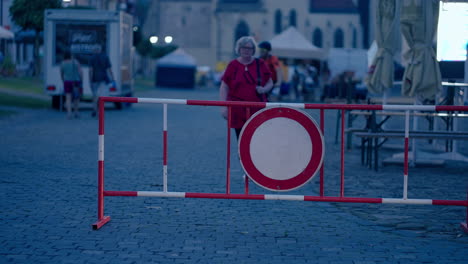 Older-Woman-approaching-Prohibition-No-Entry-Sign-and-stopping-and-doing-Gesture-With-Hands-Like-I-Don't-Know-during-a-blue-hour-at-dusk