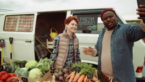 cheerful farmers video calling on smartphone at outdoor vegetable market