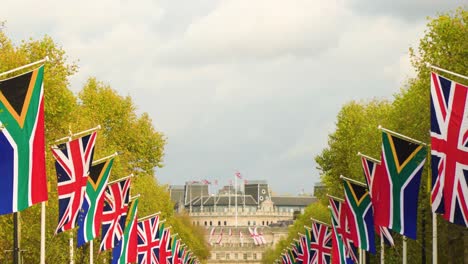 south africa and great britain united kingdom flag together hanging on a pole in line inside london with architecture buildings that carries flags on the roof vibrant tress on the sides moving clouds