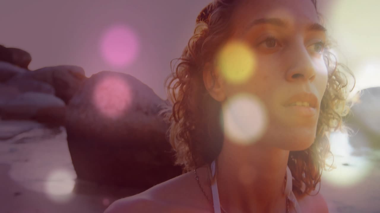 Mulher admirando pedregulhos na costa rochosa ao pôr do sol, iniciando orbes bokeh animados dançantes para design