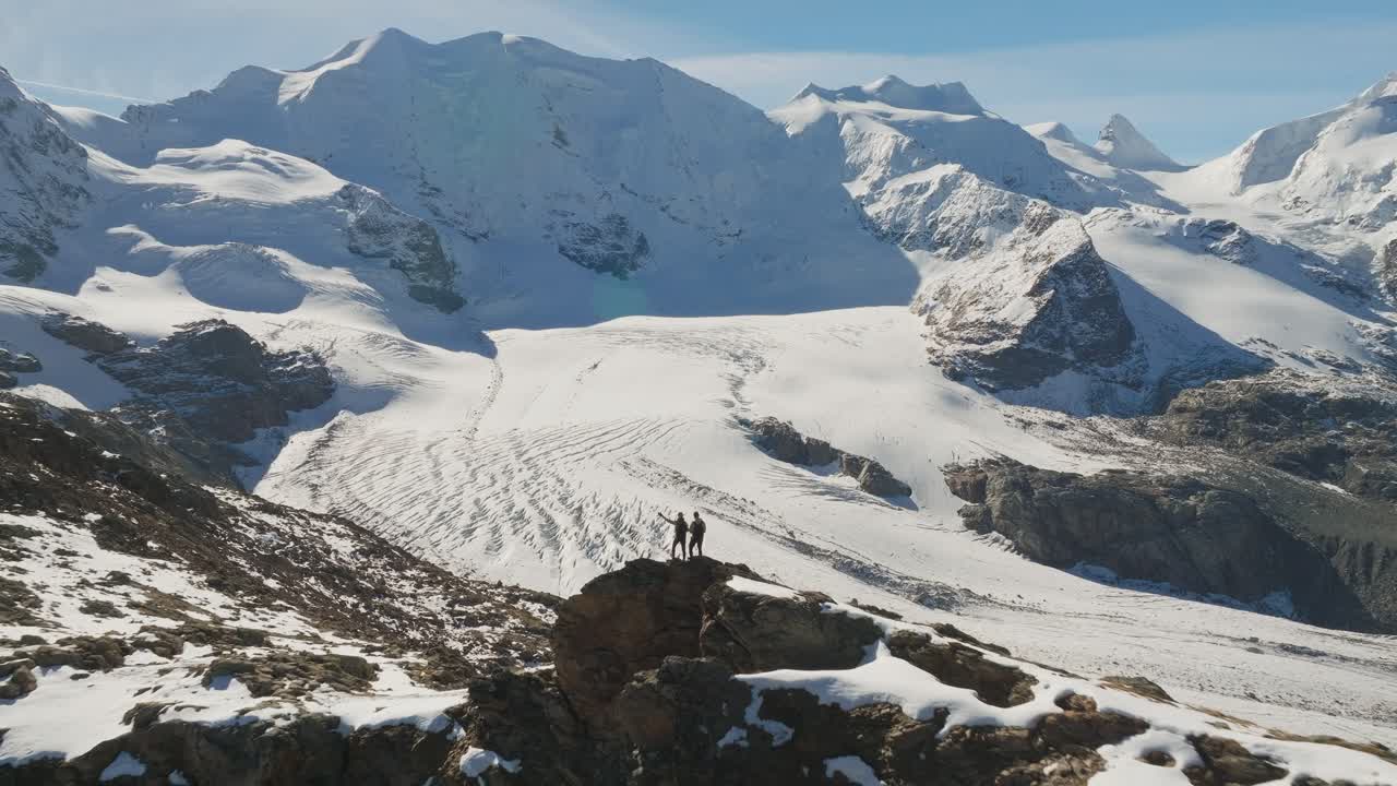 Outdoor lovers standing on rocky viewpoint overlooking large Pers Glacier
