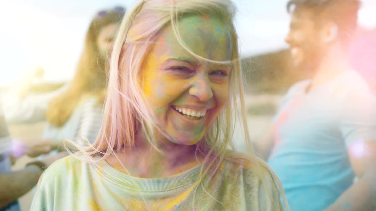 retrato en primer plano de una hermosa chica rubia bailando en celebración del festival de holi con sus amigos. su rostro y ropa están cubiertos con polvo de colores.