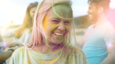 close-up portrait of a beautiful blonde girl dances in celebration of holi festival with her friends. her face and clothes are covered with colorful powder.