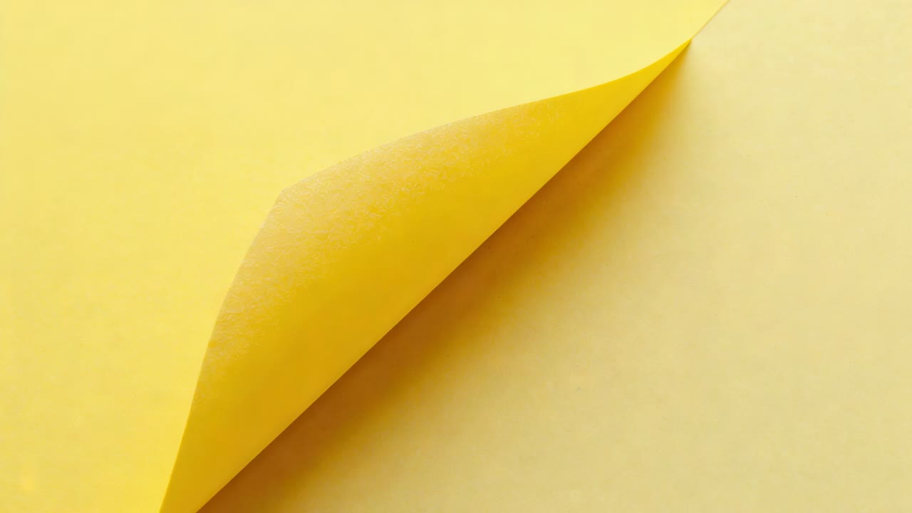 Curling yellow sheet, center lift initiating rightward peel on studio table, revealing underlayer