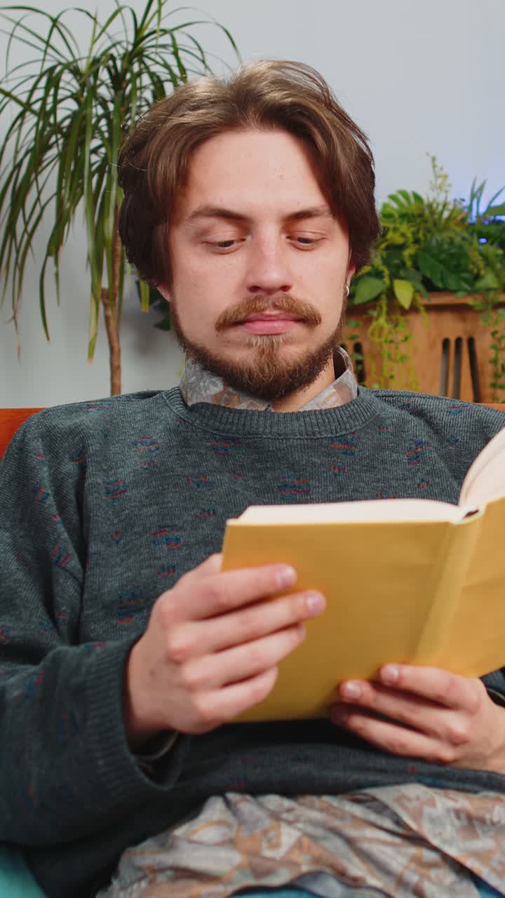 Bearded man reading interesting book turning pages smiling enjoying literature taking a rest at home