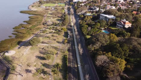 aerial tracking shot of train driving on tracks beside coastline of river plate in buenos aires