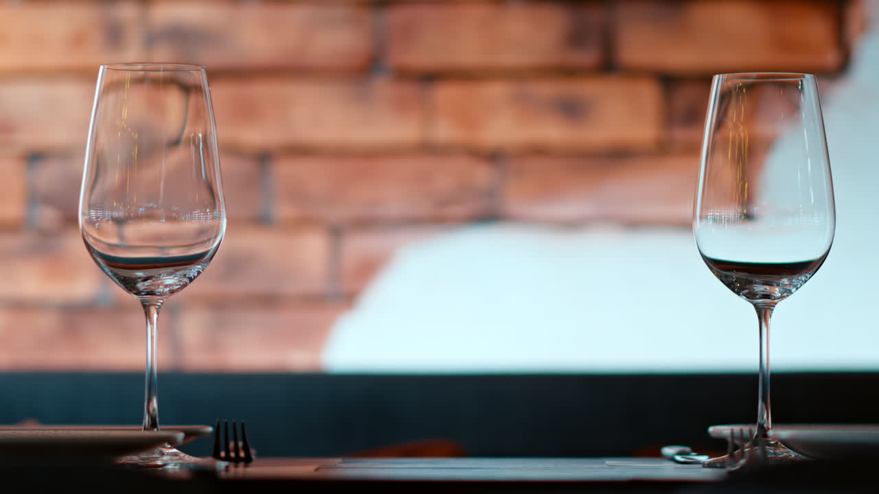 Two empty wine glasses sitting on a table at a restaurant, with a brick wall on the background