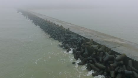 aerial establishing view of port of liepaja concrete pier, baltic sea coastline , foggy day with dense mist, moody feeling, big storm waves splashing, wide drone dolly shot moving left