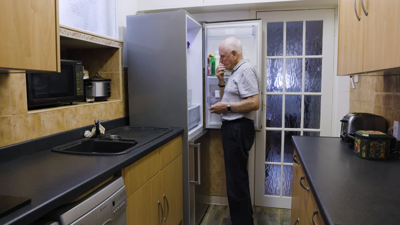 A senior man opens the refrigerator in a kitchen