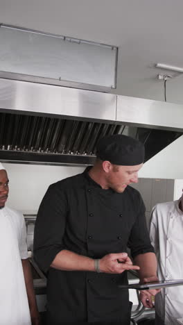 focused diverse male chef instructing trainee male chefs in kitchen, slow motion, vertical