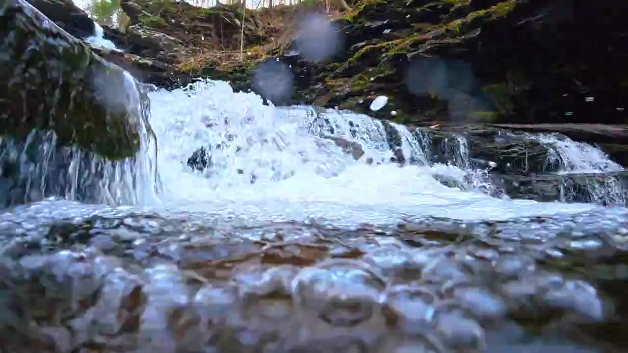 Split level view of moving water surface with bubbles. Macro shot of the interface between air and water in a flowing mountain stream.