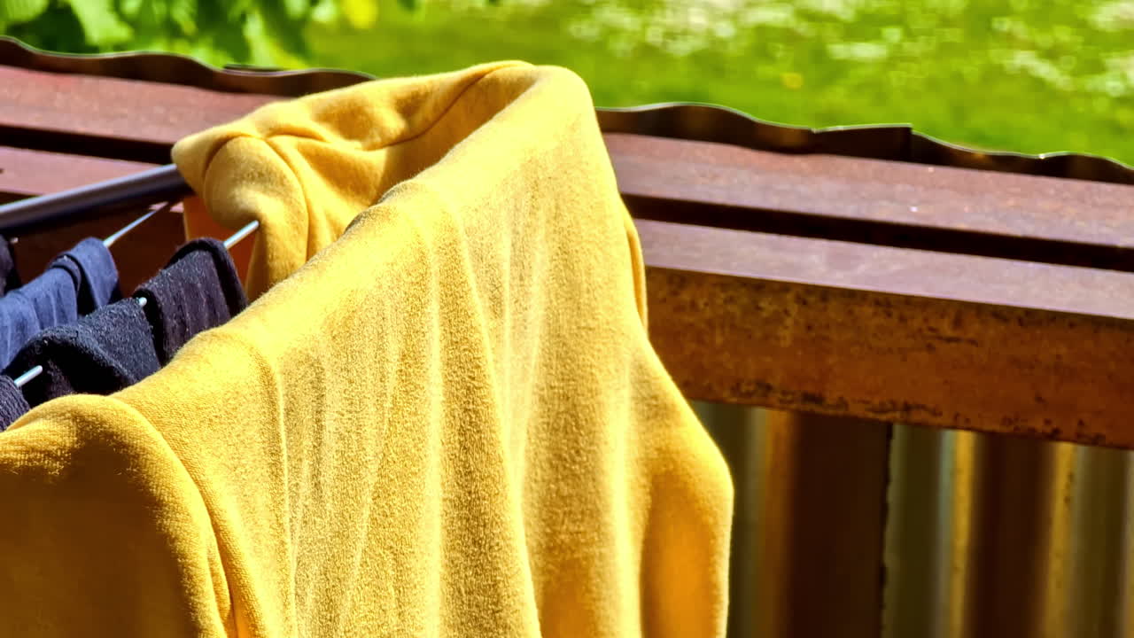 Yellow sweatshirt and dark laundry hanging to dry on balcony in sunlight