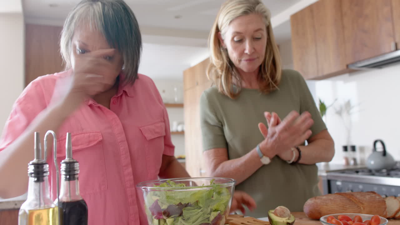 Preparing salad, multiracial senior female friends enjoying time in modern kitchen, at home